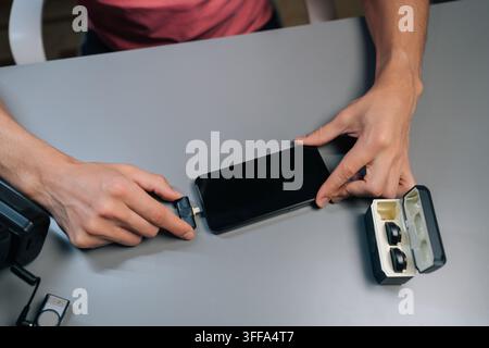 Oberansicht der Hände eines Content-Creators, der ein professionelles Audiosaufnahmesystem einrichtet, indem er den Empfänger eines drahtlosen Lavalier-Mikrofons mit Adapter an einen M anschließt Stockfoto
