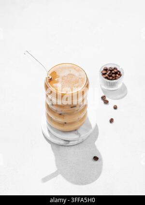 Kaltes Kaffeelatte oder Mokka in einem Glas mit Milch und Eis auf einem hellen Hintergrund mit Kaffeebohnen und Morgenschatten. Das Konzept eines sommerlichen Erfrischungsgetränks Stockfoto