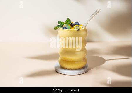 Smoothie mit Mango und Blaubeere in einem Glas auf gelbem Hintergrund mit Schatten. Gesunde Ernährung und Detox-Diät-Konzept. Vorderansicht und Kopierraum. Stockfoto