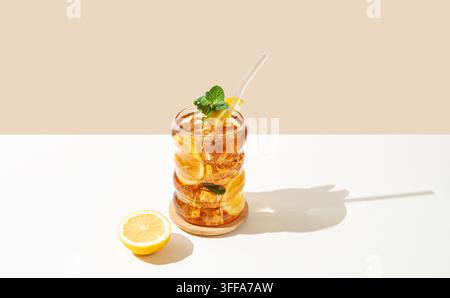 Eistee mit Zitrone, Eis und Minze in einem Glas auf Holzbrett auf weißem und beigem Hintergrund mit Schatten. Trendiges Konzept für erfrischendes Getränk oder Lemonade Stockfoto