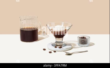 Affogato-Kaffee mit einer Kugel Vanilleeis und Espresso in einem Glas auf einem weiß-beigen Hintergrund mit Kaffeebohnen, Kanne und Schatten. Klassisch Itali Stockfoto