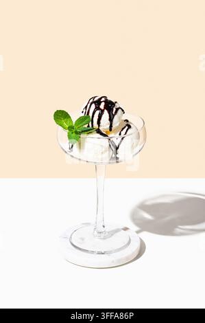 Löffel Vanilleeis in einem hohen Glas mit Schokoladenüberzug und einem Minzblatt auf hellem Hintergrund. Sommerliches erfrischendes Dessertkonzept für eine Speisekarte Stockfoto