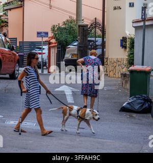 Eine ungezwungene Straßenszene in Opatija, Kroatien. Eine ältere Frau mit kurzem grauen Haar führt ihren Beagle an der Leine und blickt über ihre Schulter zurück. Eine junge Stockfoto