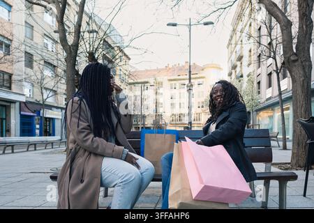 Zwei fröhliche afrikanische Frauen sitzen auf einer Bank und genießen nach einem Einkaufsbummel die gemeinsame Gesellschaft Stockfoto