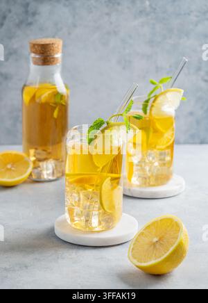 Zwei Gläser und Flasche mit gekühltem Getränk mit Zitrone und Minze auf einem hellen Hintergrund mit Schatten und Zitrusfrüchten. Das Konzept eines kalten Tees oder einer Limonade Stockfoto