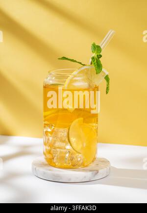 Eistee mit Zitrone und Minze in einem Glas auf einem weiß-gelben Hintergrund mit Sonnenlicht. Das Konzept eines erfrischenden Getränks oder einer Limonade an einem Sommertag. Vorderseite Stockfoto