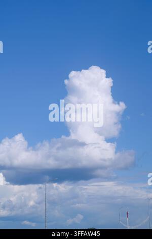 Eine auffällige Wolkenformation, die einer aufragenden Säule gegen einen klaren blauen Himmel ähnelt, mit einer bergigen Landschaft im Hintergrund. Die Szene fängt t Stockfoto