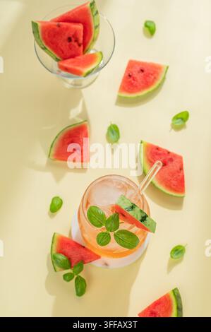 Flachlage eines Wassermelonen-Mojito-Cocktails mit Eis und Minze in einem Glas auf einem gelben Hintergrund mit frischen Scheiben und Blättern. Sommerliche erfrischende Limonade dr Stockfoto