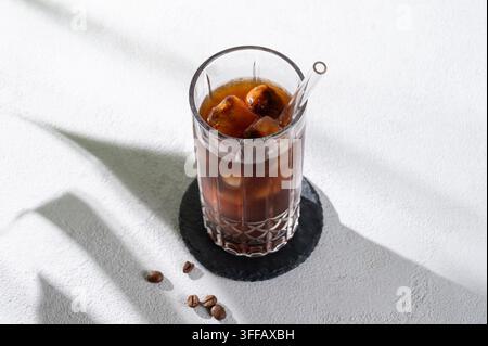 Cold Brew Kaffee-Tonic in einem Glas mit Eis auf einem hellen Hintergrund mit Kaffeebohnen und Morgenschatten. Sommerliches, erfrischendes Trendgetränkkonzept für Werbung Stockfoto