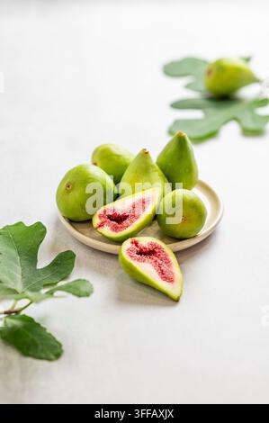 Süße grüne Feigen auf einem Teller, in Scheiben geschnitten, mit Blättern auf einem hellen Hintergrund. Konzept von saftigen und gesunden Sommerfrüchten. Kopierraum. Stockfoto