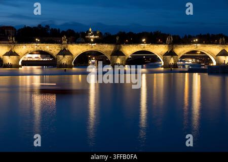 Die Nachtansicht zeigt die mittelalterlichen Brücken in Prag mit Stadtlichtern, die auf der Moldau leuchten. Stockfoto