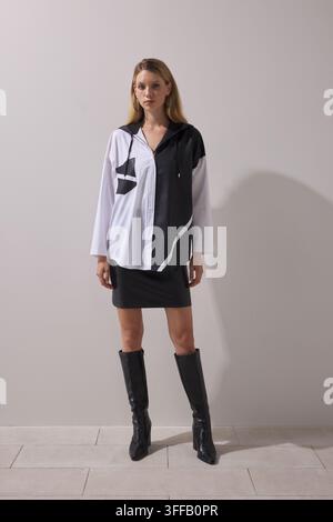 Junge blonde Frau trägt ein schwarz-weißes Colorblock-Übergroßes Hemd mit auffälligem Grafikdruckdesign, kombiniert mit einem schwarzen Minirock. Stockfoto