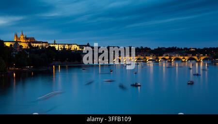 Die Szene zeigt Prag, Tschechische Republik bei Nacht mit beleuchteten Gebäuden und Booten auf dem Fluss. Stockfoto