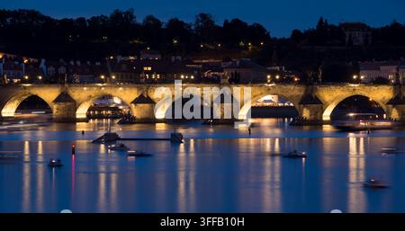 Menschen bewundern die beleuchtete Charles-Brücke in Prag, Tschechische Republik, während Boote auf dem Fluss fahren. Stockfoto