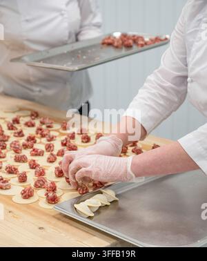 Ein Arbeiter stellt handgemachte Knödel mit roher Füllung aus Fleisch auf Metalltabletts auf einem Holztisch in einer Lebensmittelfabrik her. Konzept der traditionellen Hausmannskost Stockfoto