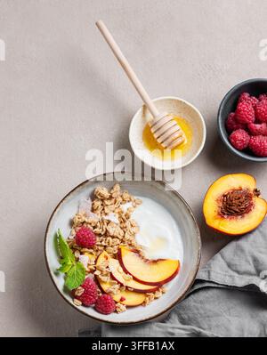 Flachlage von griechischem Naturjoghurt mit Hafergranola oder Muesli, Pfirsich, Himbeere und Honig in einer Schüssel auf hellem Hintergrund mit frischen Früchten, Beeren und Stockfoto