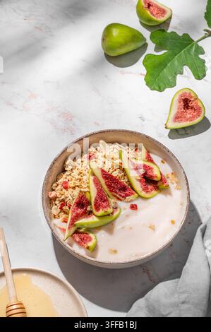 Natürlicher Joghurt mit Müsli, Feigen und Honig in einer Schüssel auf einem Marmorhintergrund mit Früchten und Morgenschatten. Konzept von gesundem und nahrhaftem Detox f Stockfoto