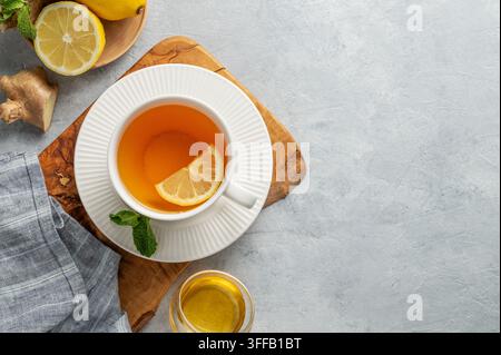 Heißer Tee mit Zitrone, Ingwer, Honig und Minze in einer Tasse auf einem Holzbrett auf hellem Hintergrund mit Zitrusfrüchten. Konzept eines Getränks zur Unterstützung der Immunabwehr Stockfoto
