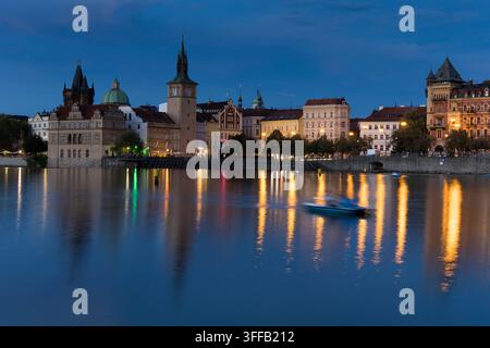 Boote bewegen sich auf dem Wasser in Prag, während Gebäude in der Dämmerung beleuchtet werden. Die Szene zeigt die Stadt bei Nacht. Stockfoto