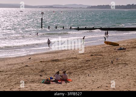 Panoramatische Ansicht des Sandstrands in Boscombe, Bournemouth, UK, mit Urlaubern, hölzernen Groynes und dem Bournemouth Pier in der Ferne. Stockfoto