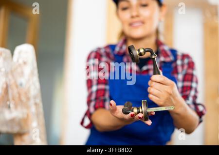 Hispanische Bauarbeiterin in Latzhose, die einen Türgriff hält. Unscharf im Hintergrund: Bauarbeiterin mit Türgriff. Stockfoto