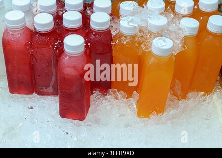 Reihen von gekühlten Rosellen- und Orangensaftflaschen in Rot- und Orangetönen, die in zerkleinertem Eis stehen, Einzelhandelsauslage für kalte Getränke, Thailand Stockfoto