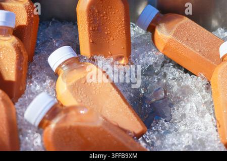 Nahaufnahme von Plastikflaschen mit Eistee, die unter hellem Sonnenlicht auf zerstoßenem Eis mit Kondenswasser bedeckt sind Stockfoto