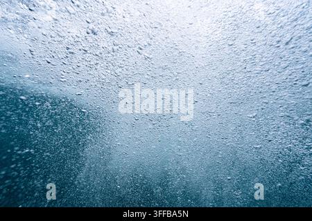 Zahlreiche Luftblasen steigen durch blaues Wasser und erzeugen einen dynamischen strukturierten Hintergrund und ein abstraktes flüssiges Muster Stockfoto