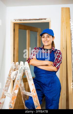 Porträt einer positiven lateinamerikanischen Bauarbeiterin, die während Renovierungsarbeiten in einer Wohnung mit verschränkten Armen steht. Stockfoto