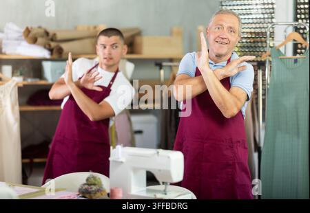 Ältere und junge männliche Schneider beim Aufwärmen während der Arbeit in der Nähwerkstatt Stockfoto
