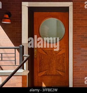 Orangefarbene Holztür mit einem großen runden Fenster und geometrischen Schnitzdetails in Chicago. Stockfoto