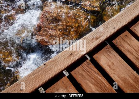 Blick von einer hölzernen Fußgängerbrücke auf klares, schnell fließendes Wasser, das 2016 in der Nähe des Luna Lake in Colorado über Felsen stürzt. Stockfoto