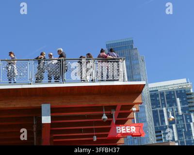 SEATTLE -18. SEP 2025 - Menschen, die sich auf einer Dachterrasse überblickend über eine moderne Stadtsilhouette unter einem klaren blauen Himmel unterhalten, genießen einen urbanen Sommernachmittag Stockfoto