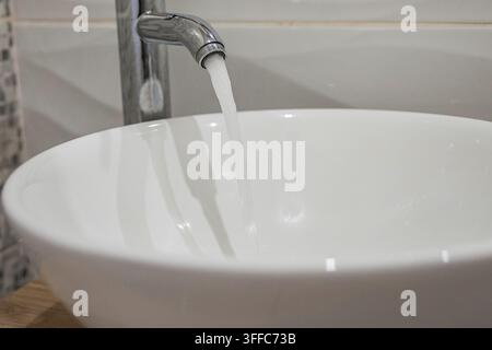 Fließendes Leitungswasser fließt in ein sauberes weißes Keramik-Waschbecken Stockfoto