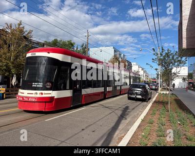 Straßenbahn der Queen Street East verkehrt entlang einer sonnigen städtischen Straße in Toronto, Ontario, Kanada, mit modernen Nahverkehrsfahrzeugen und Stadtsilhouette. Stockfoto