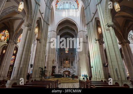 Madrid, Spanien: 7. Apr. 2025 – Gerippte gotische Bögen und lebhaft bemalte Deckenpaneele erheben sich über den Buntglas-Rosenfenstern im Langhaus der Almudena-Kathedrale Stockfoto