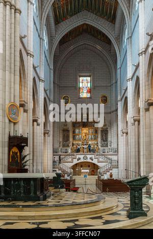 Madrid, Spanien: 7. Apr. 2025 - Das lange Marmorbasilika der Almudena-Kathedrale führt zu einem kunstvoll vergoldeten Altarbild und einem Buntglasfenster, mit ein paar Visis Stockfoto