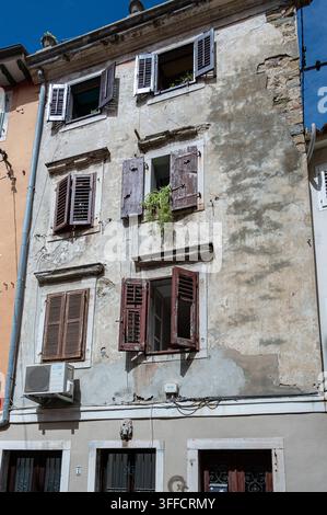 Verwitterte Fassade mit Holzläden, abblätterndem Putz und freiliegenden Kabeln in Piran, Slowenien Stockfoto