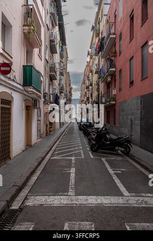 Schmale Wohnstraße in Barcelona mit Balkonen, Wäsche und geparkten Rollern Stockfoto
