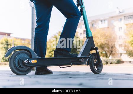 Junger Geschäftsmann im Anzug fährt einen Elektroscooter zu einem Geschäftstreffen. Ökologisches Transportkonzept. Einen E-Scooter auf der Ci mieten Stockfoto