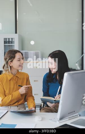 Zwei Geschäftsfrauen, die in einem modernen Bürolounge-Bereich Arbeit mit einem Laptop besprechen und Teamarbeit und Kommunikation zeigen Stockfoto