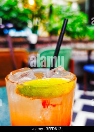 Ein erfrischender Eiskoktail, garniert mit einer Limettenscheibe und serviert mit einem Trinkhalm an einer Außenterrassenbar Stockfoto