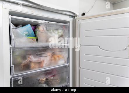 Nahaufnahme des Gefrierfachs eines Haushaltskühlschranks, zeigt die vollständigen Schubladen gefüllt mit gefrorenen Vorräten, die obere Schublade mit gebrochenem Plastikregal deutet auf ap hin Stockfoto