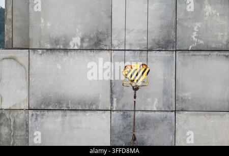 Nahaufnahme eines robusten Kranhakens mit Sicherheitsmarkierungen, der vor einem Raster aus großen Betonfertigteilen hängt, symbolisiert Stockfoto