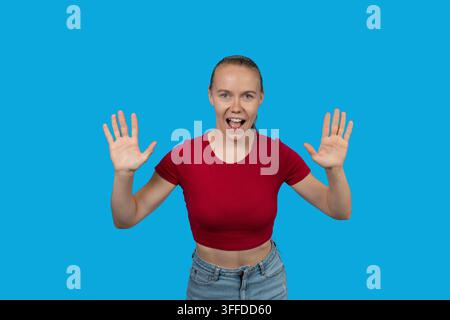 Junge Frau zeigt Begeisterung und Überraschung mit erhobenen Händen vor blauem Hintergrund Stockfoto
