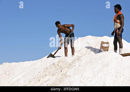 Zwei Salzarbeiter arbeiten auf einem weißen Salzberg in der Danakil-Senke, Afar, Äthiopien, mit traditionellen Handwerkzeugen unter einem klaren blauen Himmel. Stockfoto