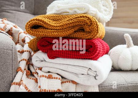 Gemütlicher Herbstheimkomfort, Stapel warmer Strickdecken und Pullover auf einem Sofa mit saisonalem Dekor für Herbstinneneinrichtung und Entspannung Stockfoto