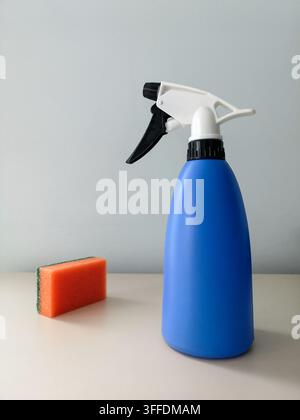 Reinigung und Desinfektion der Räumlichkeiten. Orangefarbener Schwamm und blauer Sprüher auf einem Tisch an einer hellen Wand Stockfoto