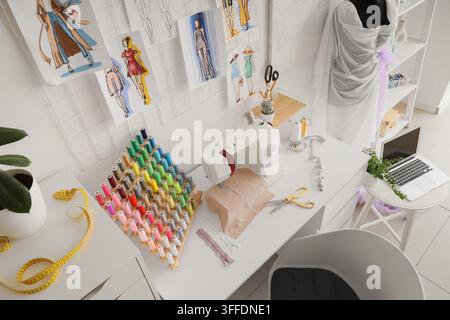 Nähmaschine mit Stoff und Garnspulen auf dem Schneiderisch im Atelier Stockfoto