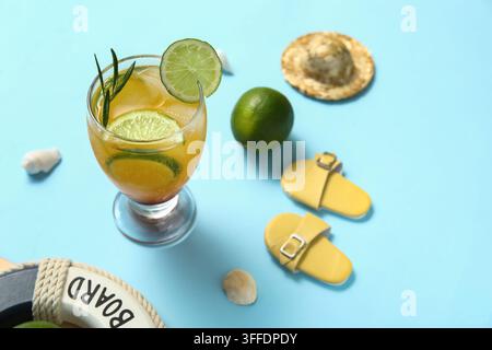 Glas mit leckerem Cocktail mit Limette, Flip-Flops, Rettungsring, Muscheln und Strohhut auf blauem Hintergrund Stockfoto